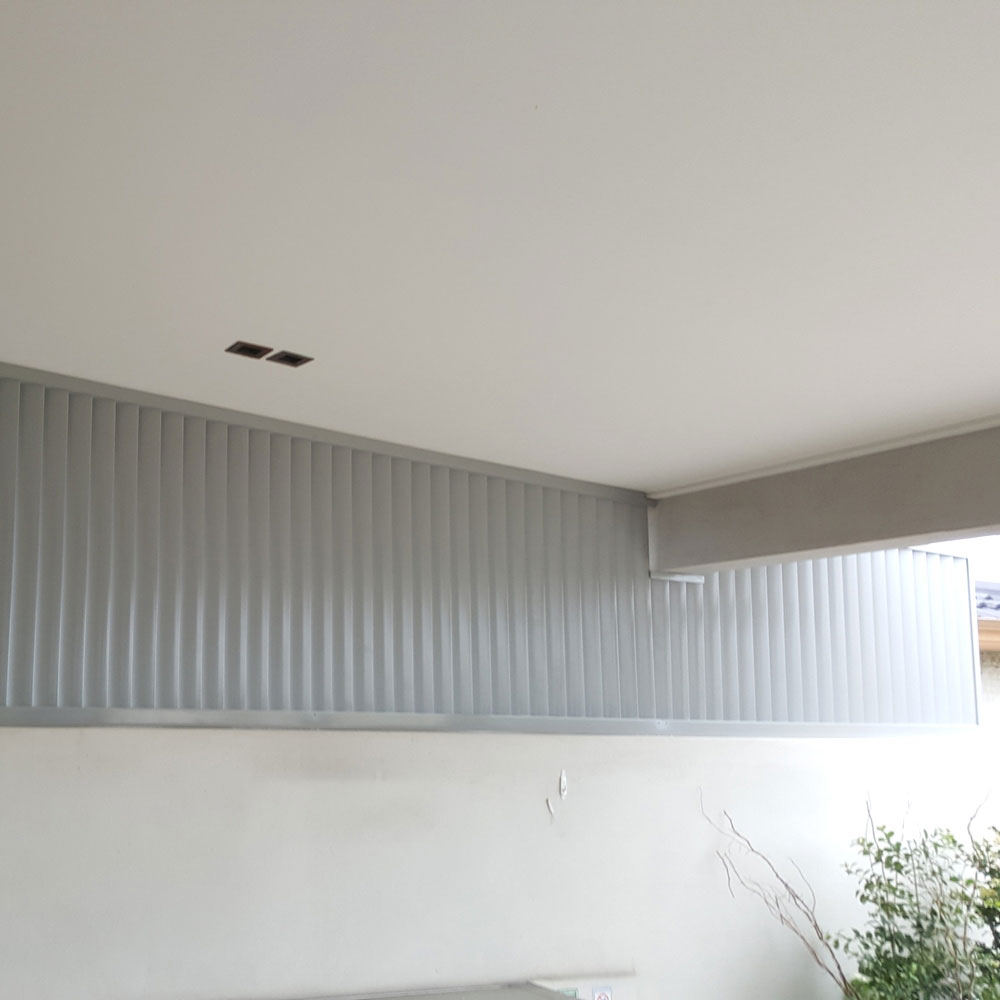 Vertical 160 mm aluminium louvres installed along a veranda wall, custom-cut to match the angled roofline for full enclosure and privacy.