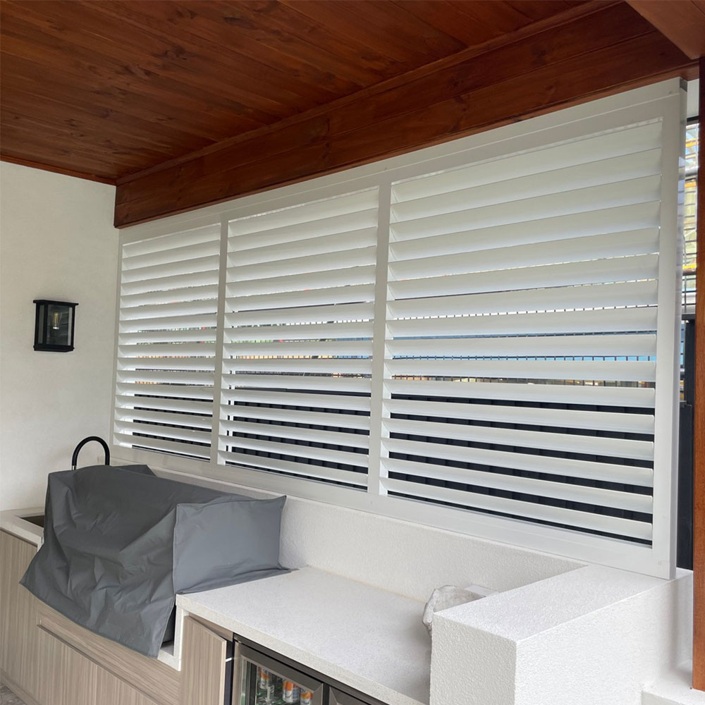 Horizontal 85 mm adjustable aluminium louvres installed behind an outdoor BBQ area, providing privacy, airflow control, and sun shading.