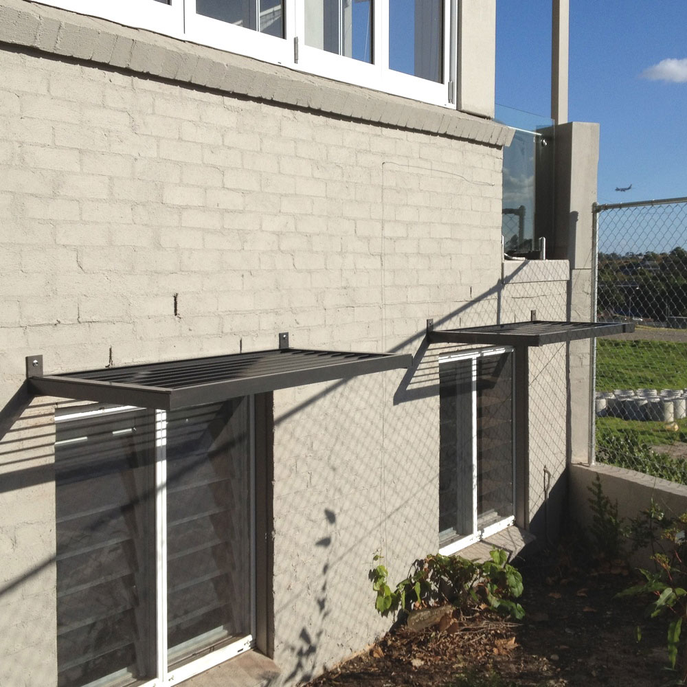 Cantilever aluminium louvre awnings installed above lower-level windows on a rendered brick wall.