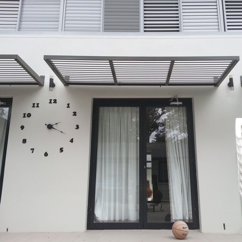 Cantilever aluminium louvre awning installed above black-framed sliding doors on a modern white façade.