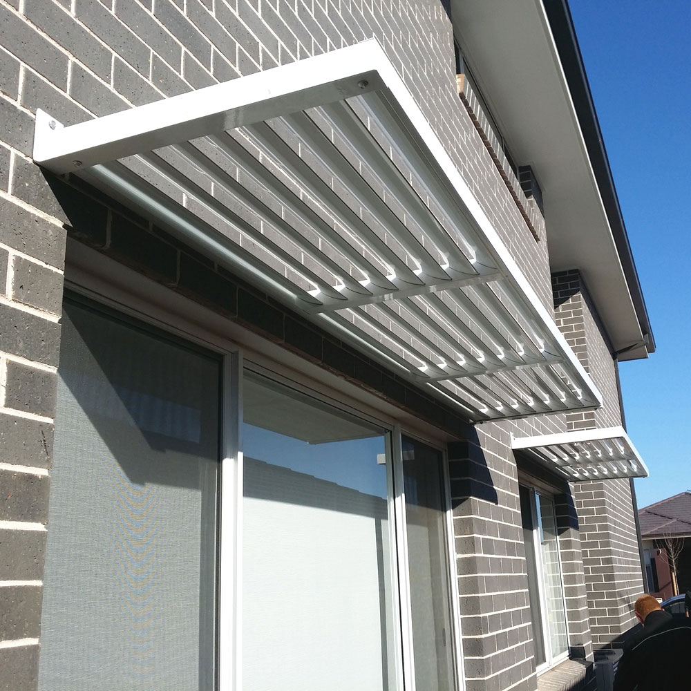 Cantilever aluminium louvre awnings installed above upper-storey windows on a modern brick home.