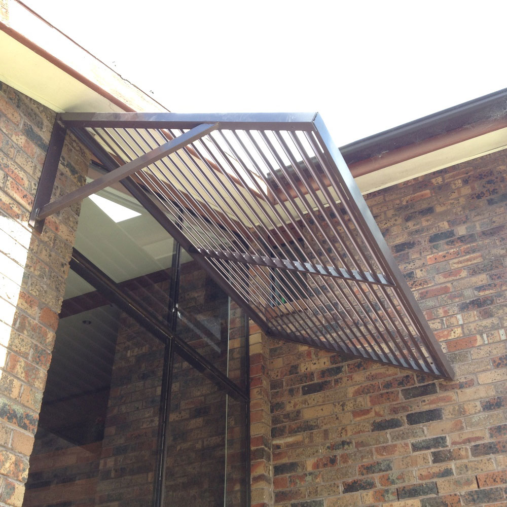 Cantilever aluminium louvre awning with support arm installed above a brick façade and large glass windows.