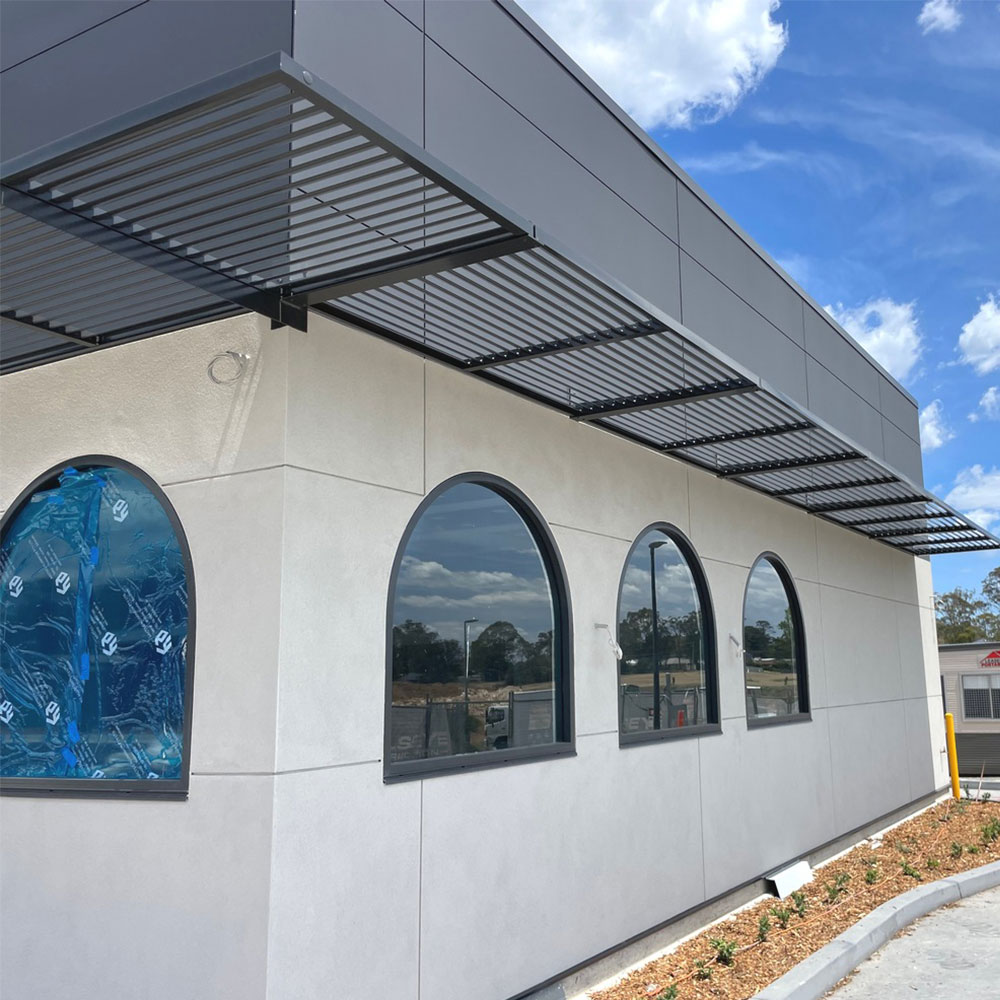 Cantilever aluminium louvre awnings wrapping around a commercial building façade with evenly spaced horizontal blades.