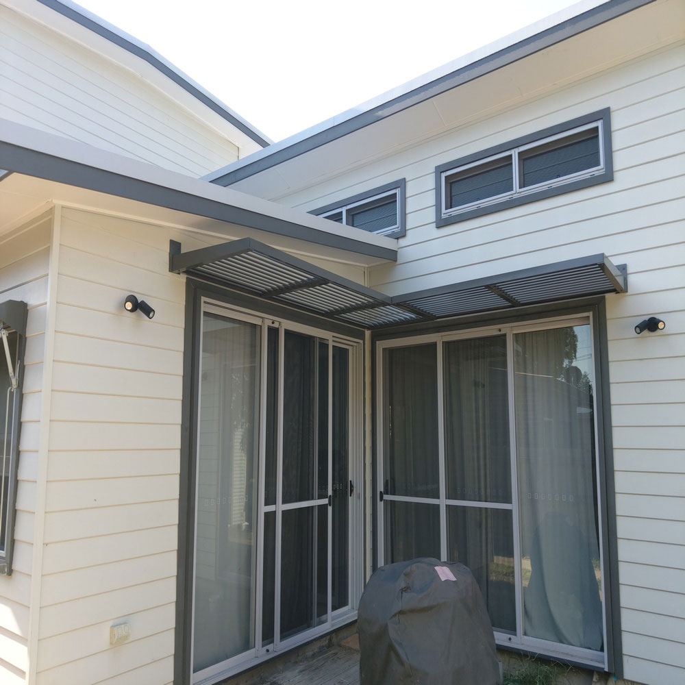 Corner cantilever aluminium louvre awning with horizontal blades installed over sliding doors on a modern home.