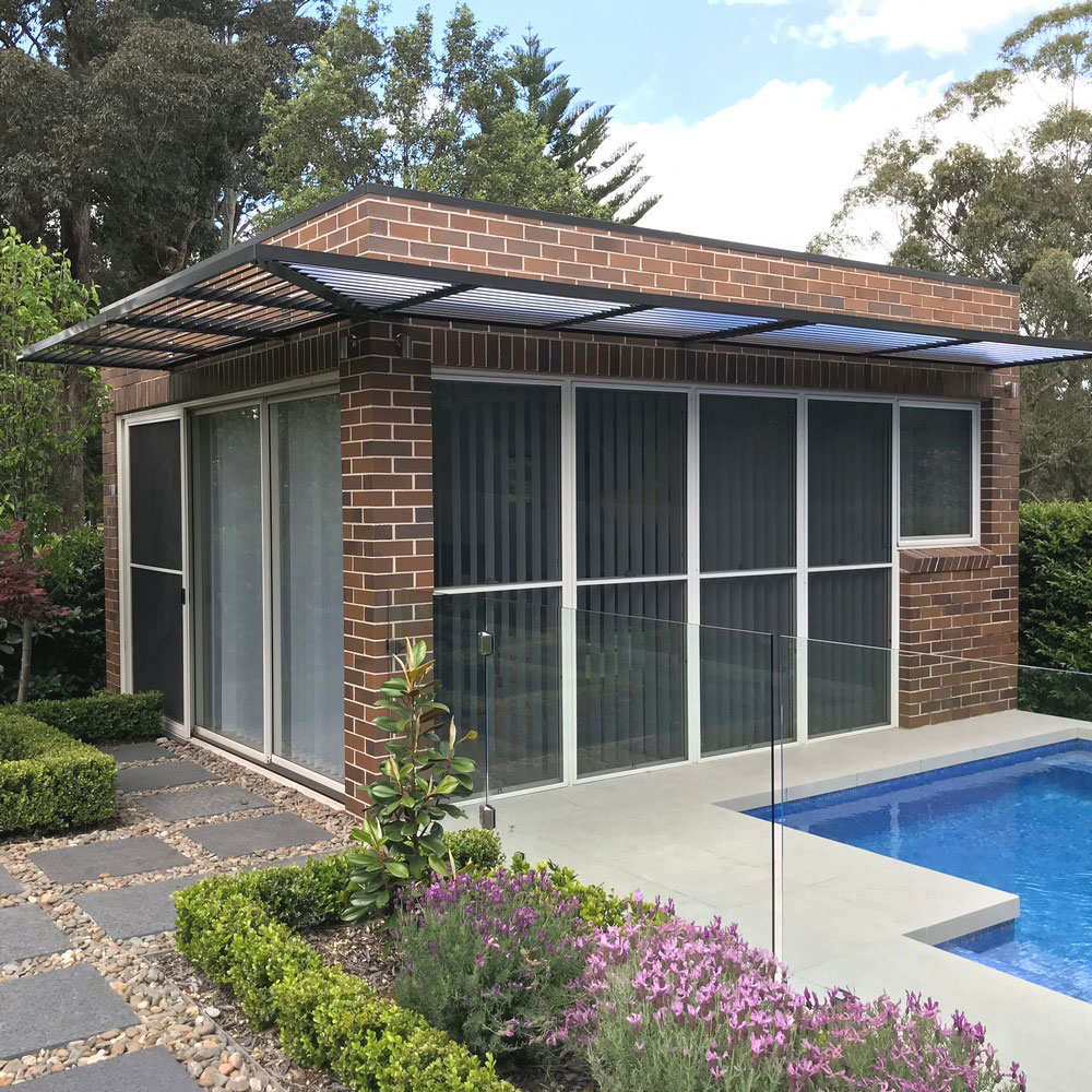 Cantilevered aluminium louvre awning with an outside mitred corner installed around a brick poolside building.