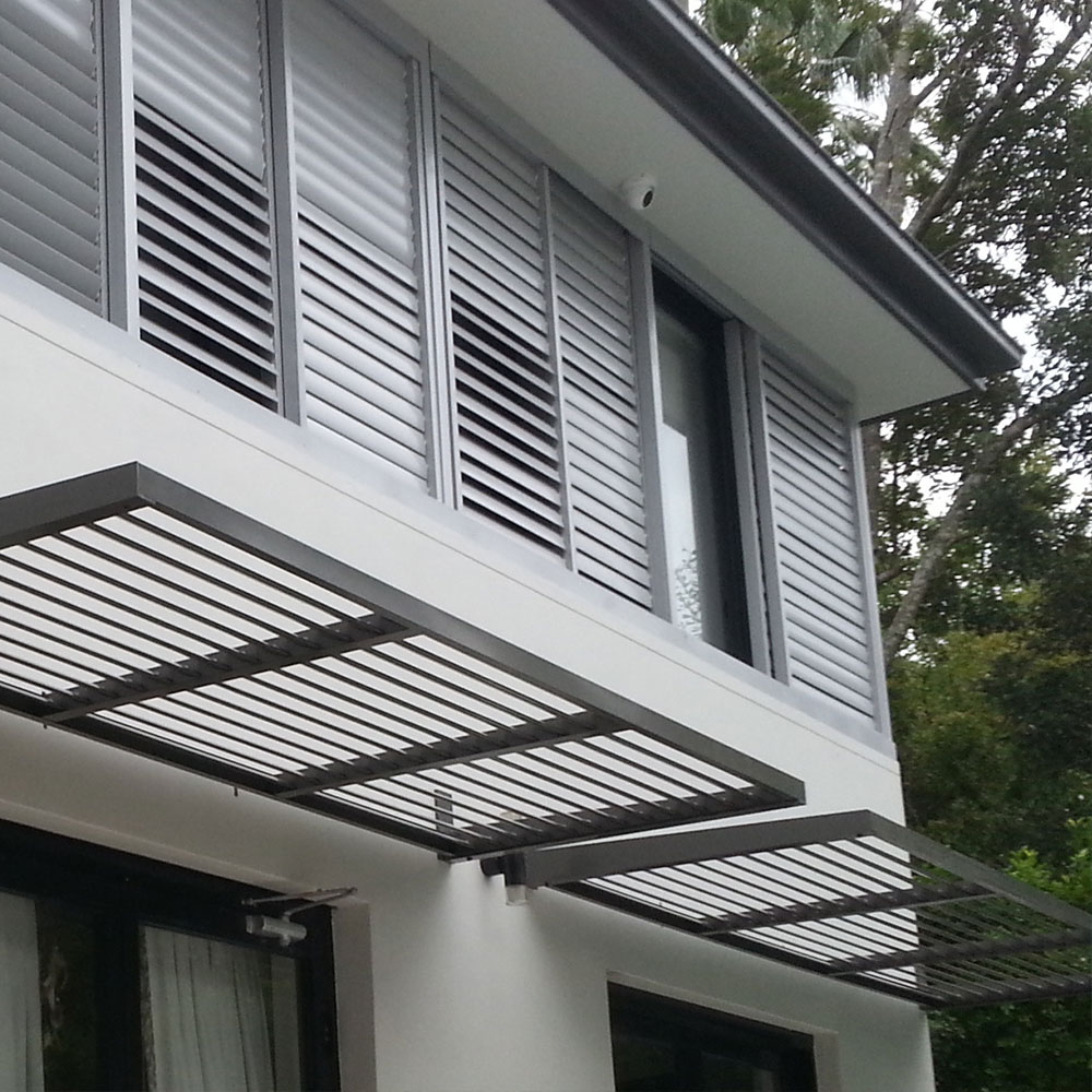 Cantilever aluminium louvre awnings installed above lower-storey windows on a modern two-storey home with matching upper louvre shutters.