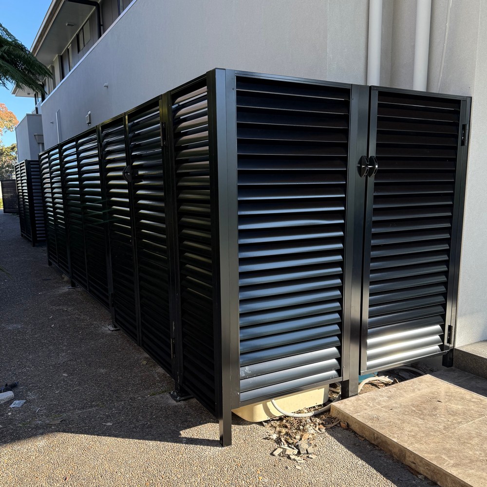 Black aluminium louvre enclosure with gates housing pool pump and air conditioning units along a side access path