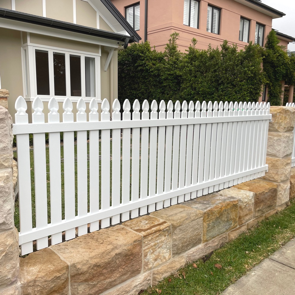White aluminium picket fence with vertical slats and decorative pointed tops mounted on a sandstone boundary wall