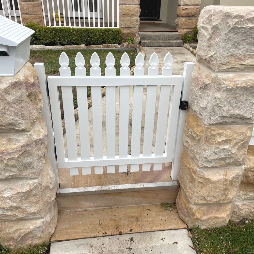 White aluminium picket front gate installed between stone pillars at a residential entrance.